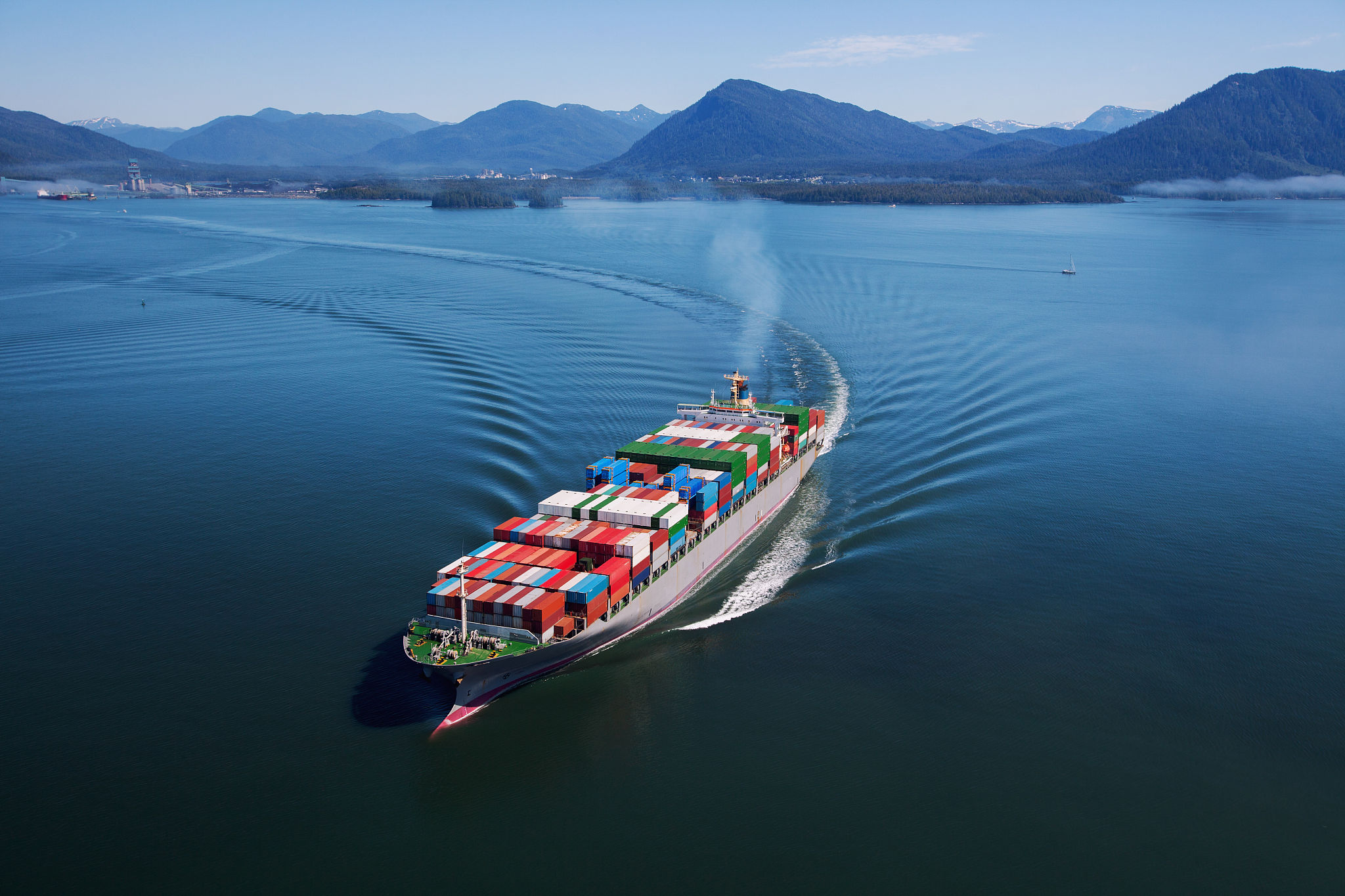 Shipping containers stacked at a port with a cargo ship in the background